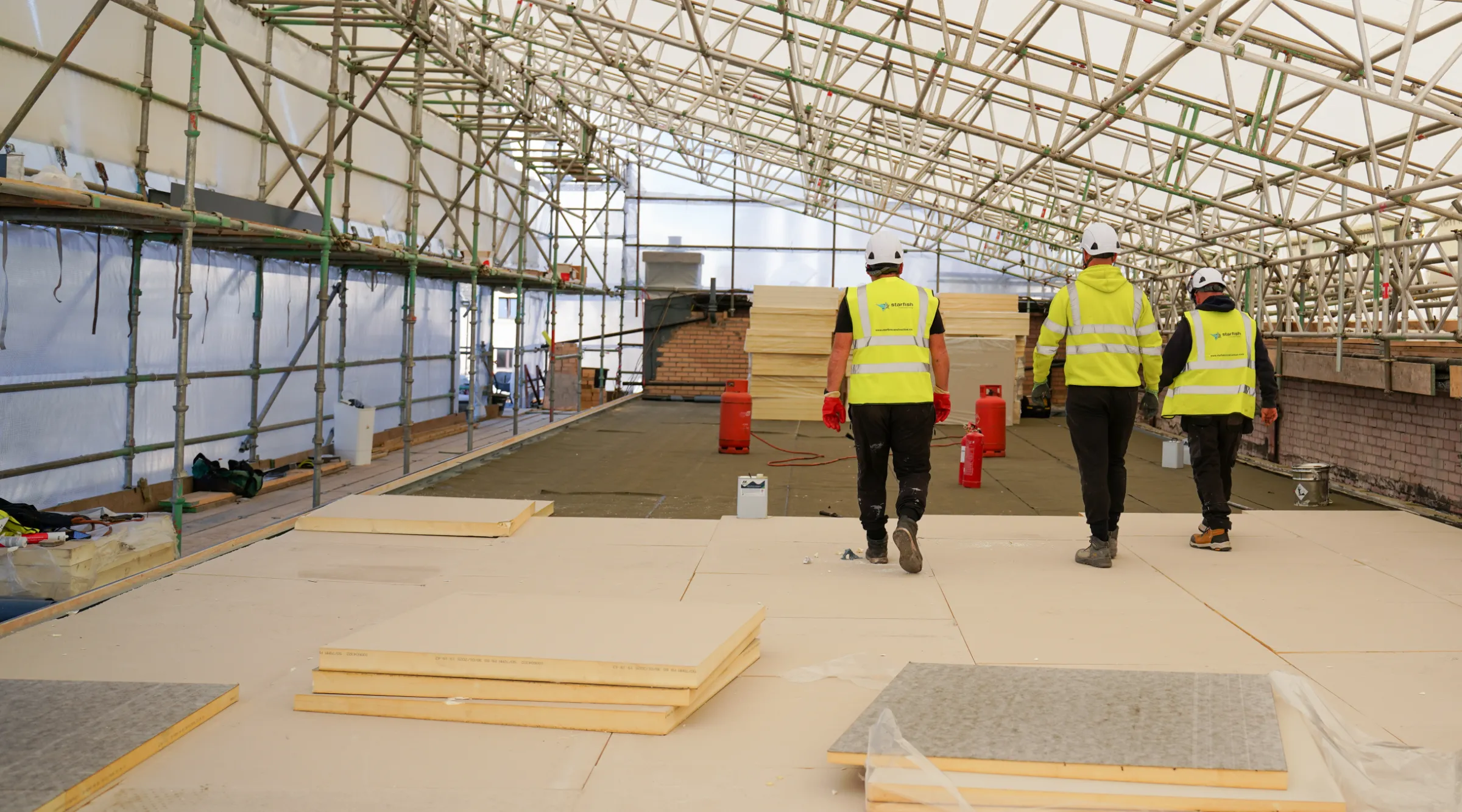Starfish Construction team walking across a new roof deck under a temporary roof enclosure during RAAC remediation in Leith, Edinburgh