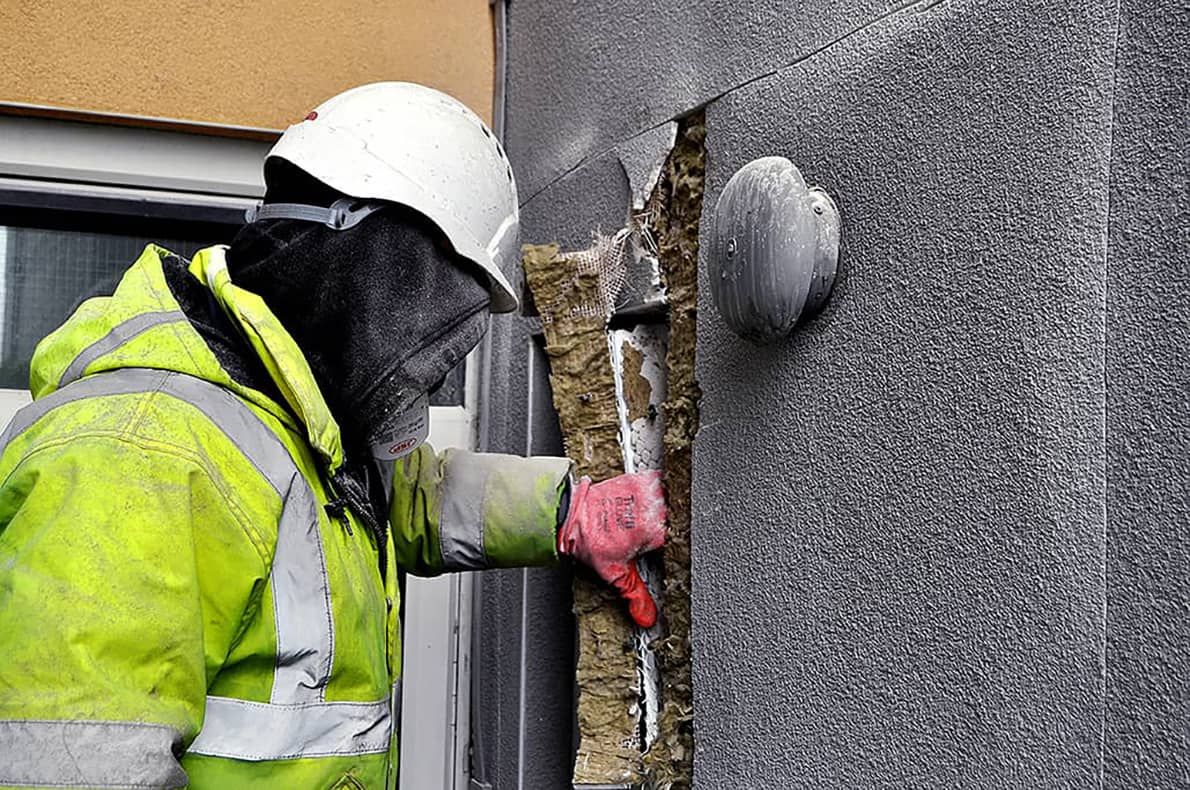 person in PPE removing material from a building exterior