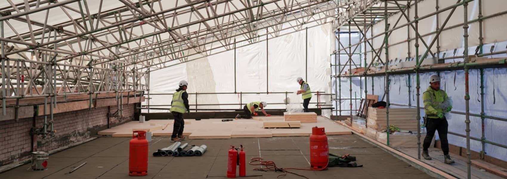Scaffolding within enclosed work area with work people laying flooring