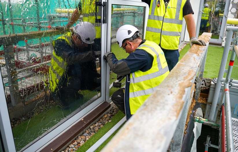 building showing scaffolding and green netting surrounded by trees