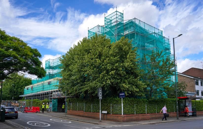 building showing scaffolding and green netting surrounded by trees